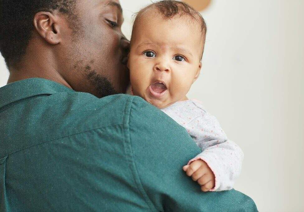 Back view portrait of young African-American father holding son with cute baby looking at camera over mans shoulder, copy space