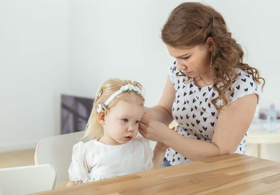 Mother helps to put on cochlear implant for her deaf little daughter. Hearing aid and deafness